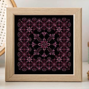 Op de afbeelding: Vierkant ingelijst kunstwerk met een symmetrisch bloemmotief in roze tinten op een zwarte achtergrond. Het kunstwerk wordt gepresenteerd in een lichtgekleurde houten lijst. Het ontwerp is gedetailleerd en decoratief, geschikt voor interieurdecoratie.