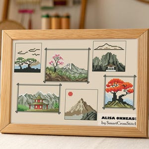 Op de afbeelding: Een ingelijst kruissteekkunstwerk met zes panelen van Japanse landschappen. De panelen tonen bergen, bomen en een pagode, allemaal in gedetailleerde kruissteek. De lijst is van lichtgekleurd hout. De tekst "ALISA OKNEAS by SmartCrossStitch" is zichtbaar.