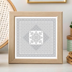 May include: Square framed art print featuring a detailed black and white geometric design. The artwork has a central floral motif and a patterned border. The frame is made of light-colored wood, and the print is displayed on a white surface.