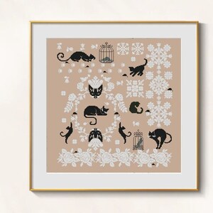 May include: Cross-stitch artwork in a gold frame, depicting black cats, mice, and birdcages on a tan backdrop. White floral and snowflake motifs are arranged around the central figures. The piece has a vintage aesthetic.