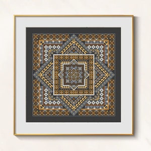May include: Framed cross-stitch artwork featuring a geometric design in shades of brown, gold, gray, and white on a dark gray background. The artwork is square and framed in a gold-colored frame, creating a decorative piece.