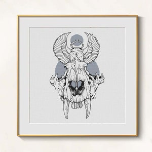 Könnte beinhalten: Schwarz-Weiß-Illustration eines Schädels mit Flügeln und einem Käfer-Design, gerahmt in einem goldenen Rahmen. Das Kunstwerk ist ein Kreuzstichmuster mit hellgrauem Hintergrund.