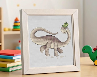 Può includere: Un ricamo a punto croce incorniciato di un simpatico dinosauro con un cappello verde. Il dinosauro è raffigurato in tonalità marroni e beige, su uno sfondo grigio chiaro. La cornice è in legno chiaro.