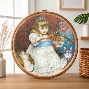 Puede incluir: Un bordado de punto de cruz de una niña tocando el violín, rodeada por un perro y un gato. La obra de arte está enmarcada en un aro de madera, con un diseño detallado que presenta un lazo y una faja azules. El fondo tiene un tono rojizo-marrón.