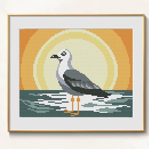 Può includere: Opera a punto croce di un gabbiano sull'acqua, con un tramonto sullo sfondo. Il gabbiano è grigio e bianco, con zampe arancioni e becco nero. Il tramonto è una sfumatura di giallo e arancione.
