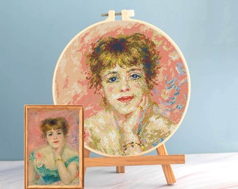 Pode incluir: Uma pintura emoldurada e um retrato em ponto cruz de uma mulher com olhos azuis e lábios vermelhos. O ponto cruz está num bastidor de madeira, e a pintura numa moldura de madeira. Ambos os retratos estão num cavalete de madeira sobre um fundo azul claro.