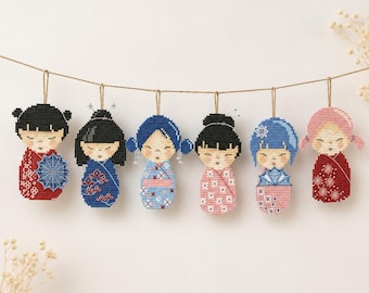 May include: A garland of six hanging ornaments featuring stylized figures with closed eyes and patterned clothing. The figures are rendered in a beaded or cross-stitch style, suspended from a thin brown string against a plain background.