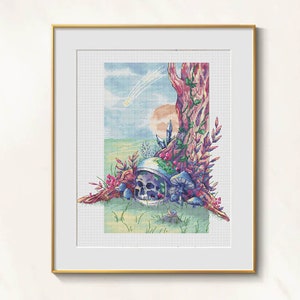 May include: Cross-stitch art framed in gold. The artwork depicts a skull inside a space helmet, nestled under a tree with mushrooms and crystals. A comet streaks across a blue sky with a setting sun. The scene is set in a grassy field.