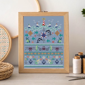 May include: Cross-stitch picture in a wooden frame with a nautical theme. The design includes a lighthouse, sailboats, dolphins, mermaids, anchors, and various sea creatures in shades of blue, green, and red.