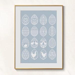 May include: Framed artwork featuring a light blue background with 15 white cross-stitch Easter egg designs. Each egg has a unique pattern, including geometric shapes, bunnies, and chickens. The artwork is in a gold frame.