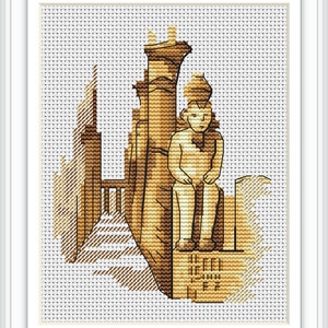 May include: Cross-stitch artwork depicting an ancient Egyptian statue and architecture in shades of brown and tan. The artwork features a seated figure and detailed architectural elements, framed in white.