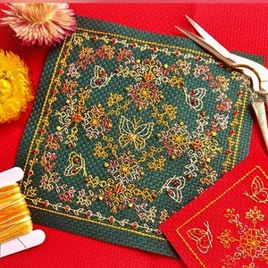Op de afbeelding: Een gedetailleerd kruissteekborduurwerk met een donkergroene achtergrond, met vlinder- en bloemmotieven in geel, oranje en rood. Een klein rood vierkant met een vlindermotief is ook zichtbaar. Gouden schaar en draad zijn inbegrepen.