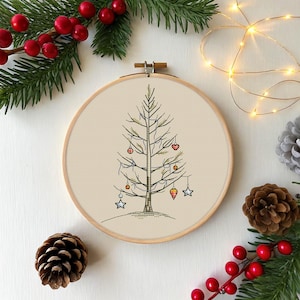 Può includere: Un telaio ricamato a mano con un design minimalista di albero di Natale. L'albero è adornato con piccoli ornamenti rossi, arancioni e blu. Il ricamo è su un tessuto neutro, incorniciato da un cerchio di legno e circondato da decorazioni festive.