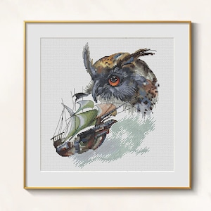 May include: Cross-stitch artwork of an owl and a ship. The owl has brown, black, and blue feathers with an orange eye. The ship has green and brown sails. The artwork is framed in a gold frame.