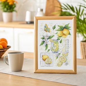 Puede incluir: Una obra de arte en punto de cruz enmarcada con limones, una mariposa y un vaso de limonada. La obra de arte está en un marco de madera y está colocada sobre una mesa con una taza de color neutro y una cesta de naranjas en el fondo.