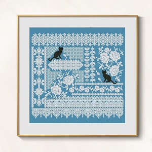 May include: Cross-stitch artwork with a blue backdrop, showcasing white floral and geometric patterns. Two black cat silhouettes are featured in the design. The artwork is presented in a gold-coloured frame.