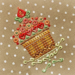 May include: Embroidered cupcake design with red, orange, and green thread on tan fabric with white polka dots. The cupcake features a detailed basket, hearts, and floral accents, showcasing a handcrafted aesthetic.