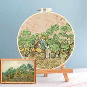 Könnte beinhalten: Ein Kreuzstich-Stickrahmen mit einer detaillierten Darstellung einer Landschaft mit Figuren, die Oliven ernten, inspiriert von Van Goghs Kunstwerk. Ein gerahmter Druck des Originalgemäldes wird vor der Stickerei ausgestellt.
