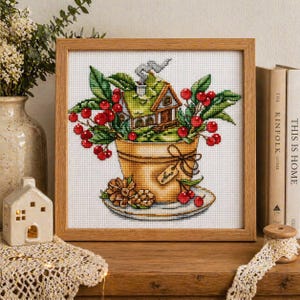 Könnte beinhalten: Kreuzstich-Kunstwerk in einem Holzrahmen. Das Kunstwerk zeigt ein Haus in einer dekorativen Tasse mit roten Beeren und grünen Blättern. Ein Tannenzapfen und ein Etikett sind ebenfalls zu sehen. Die Farbpalette umfasst Brauntöne, Grün und Rot.