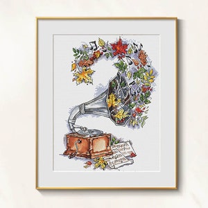 May include: Cross-stitch art of a vintage gramophone with autumn leaves and musical notes. The gramophone is silver and brown, with a detailed design. The artwork is framed in a gold frame.