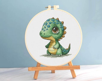 Può includere: Un punto croce di un dinosauro dei cartoni animati in un telaio da ricamo in legno. Il dinosauro è verde e giallo con macchie blu e grandi occhi marroni. Il telaio è esposto su un piccolo cavalletto di legno.