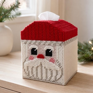 Può includere: Un copriscatola per fazzoletti quadrato realizzato in tela di plastica con un tetto rosso e un design a forma di volto di Babbo Natale. Il volto presenta occhi neri, un naso rosso, guance rosa e una barba bianca. Un fazzoletto bianco sporge dall'apertura superiore.