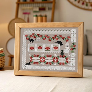 May include: Framed cross-stitch art with a beige background, showcasing a floral and cat design. The design incorporates red roses, white lace, and black cat silhouettes. The wooden frame provides a rustic aesthetic to the artwork.