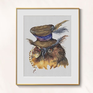 May include: Cross-stitch artwork of an owl wearing a brown top hat with a blue band and a monocle. The owl has brown and gold feathers, and the artwork is framed in a gold-colored frame.