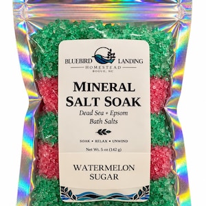 May include: A holographic pouch filled with alternating layers of green and pink mineral salt soak. The label reads Bluebird Landing Homestead Bogue, NC, Mineral Salt Soak, Dead Sea + Epsom Bath Salts, Soak Relax Unwind, Net Wt. 5 oz, Watermelon Sugar.