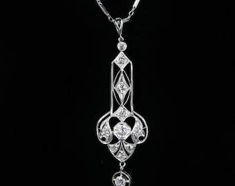 May include: A silver pendant necklace with a geometric design. The pendant features multiple round and diamond-shaped clear stones. The necklace has a delicate chain with small, round stones spaced along it. The background is black.