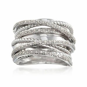 May include: A wide silver-toned ring featuring multiple overlapping bands. The design consists of alternating smooth polished bands, twisted rope-textured bands, and bands encrusted with small, clear, sparkling stones in a multi-row arrangement.