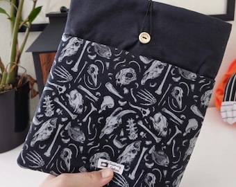 May include: Black fabric zippered pouch with a white and grey print of bones and skulls. The pouch has a black button closure and a small label that reads "Rosemary Collection".