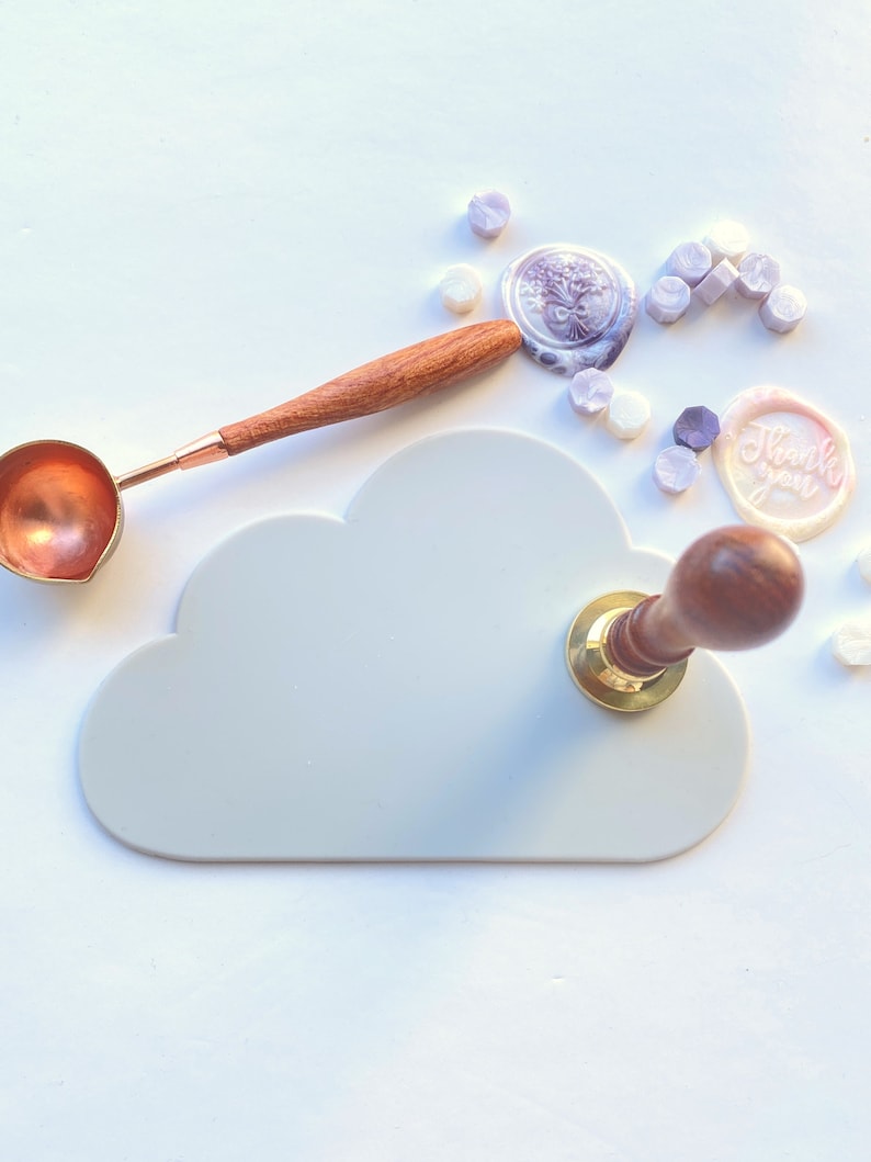 May include: A white cloud-shaped silicone mat with a wooden and gold wax seal stamp on top. The mat is surrounded by purple and white wax seals, including one that says "Thank you".