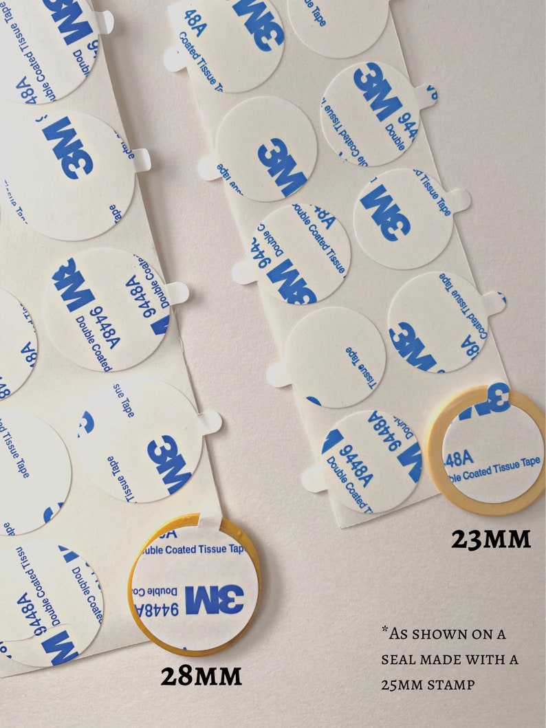 May include: Close-up of two different sizes of round, white, adhesive 3M double-coated tissue tape. The larger tape is 28mm in diameter and the smaller tape is 23mm in diameter. The text "AS SHOWN ON A SEAL MADE WITH A 25MM STAMP" is printed below the tape.
