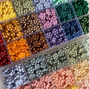 May include: A close-up view of a storage box filled with various colors of small flower-shaped beads. The beads are arranged in rows and columns, creating a colorful and organized display.