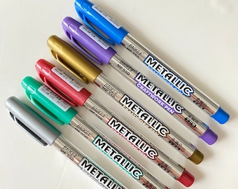 May include: A set of six metallic markers with silver caps. The markers are labeled "BAOKE METALLIC CRAFTWORK PEN" and have the text "金属色" in Japanese. The markers are in the colors silver, green, red, gold, purple, and blue.