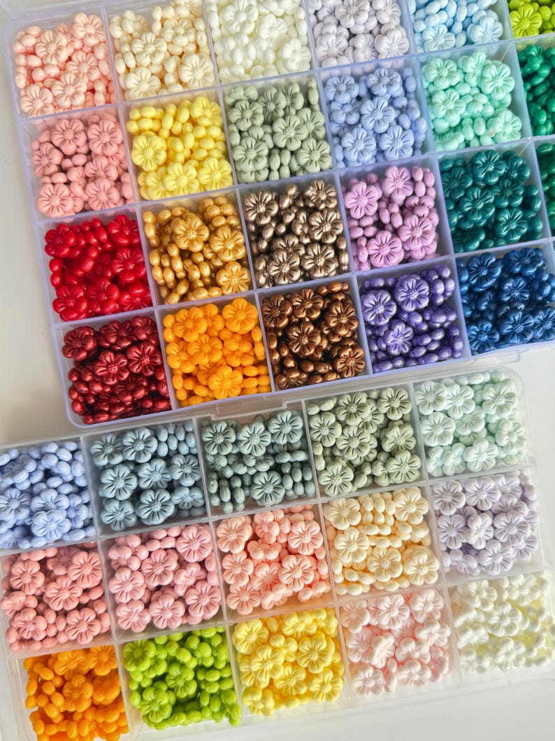 May include: A clear plastic storage box filled with small flower-shaped beads in various colors, including red, orange, yellow, green, blue, purple, and white.