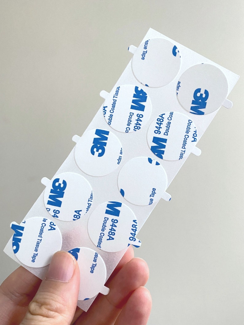 May include: A sheet of white adhesive tape with blue 3M branding and the text "Double Coated Tissue Tape" and "9448A" printed on each circle.
