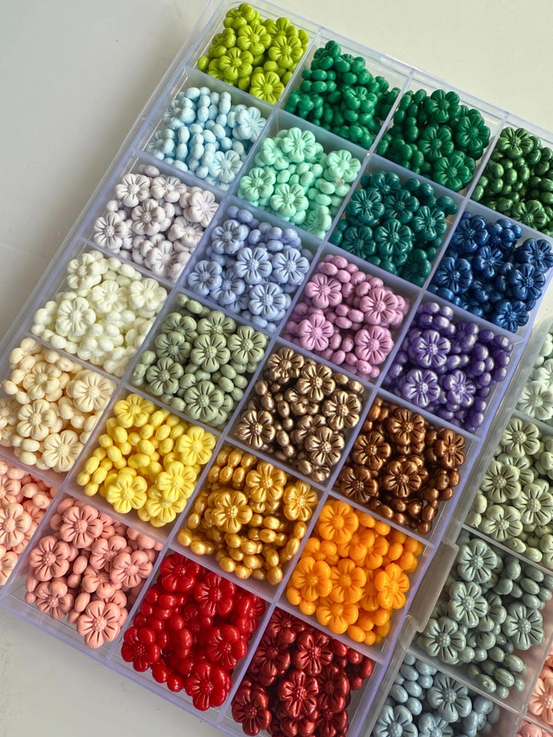 May include: A clear plastic storage box filled with small flower-shaped beads in various colors, including green, blue, purple, white, yellow, orange, red, and brown.