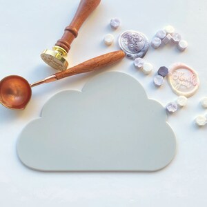 May include: A white cloud-shaped silicone mat for sealing wax, with a wooden handle wax stamp, a copper spoon, and a variety of colorful wax seals. The wax seals have different designs, including a floral design and the words "Thank you".