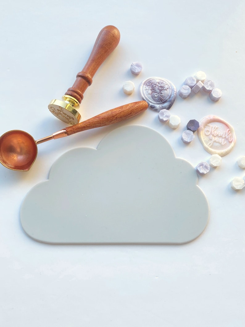 May include: A white cloud-shaped silicone mat for sealing wax, with a wooden handle wax stamp, a copper spoon, and a variety of colorful wax seals. The wax seals have different designs, including a floral design and the words "Thank you".
