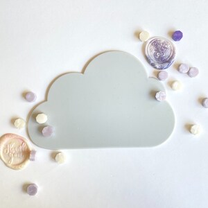 May include: A gray cloud-shaped silicone tray with a variety of purple and white wax seals scattered around it. The seals have different designs, including a floral design and the words "Thank you".