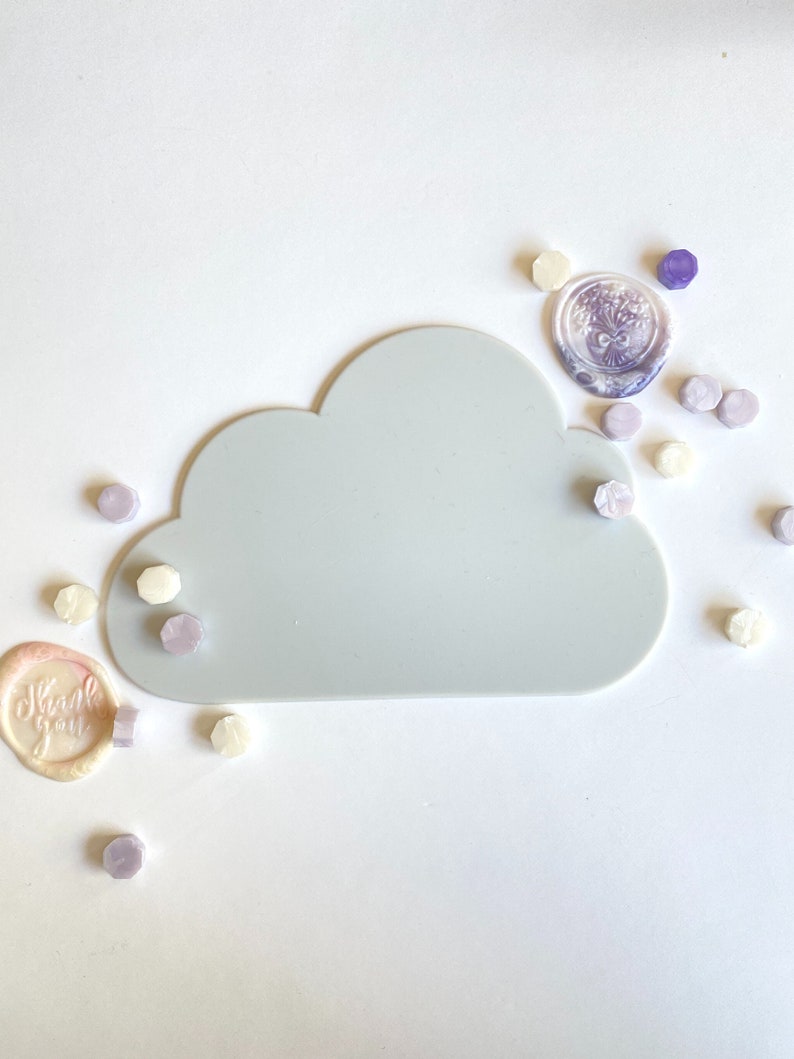 May include: A gray cloud-shaped silicone tray with a variety of purple and white wax seals scattered around it. The seals have different designs, including a floral design and the words "Thank you".