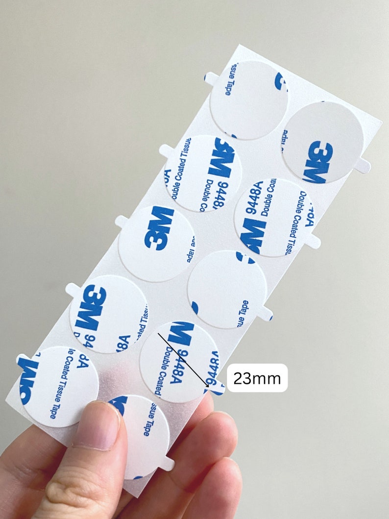 May include: A sheet of 3M double-coated tissue tape with 23mm diameter circles. The tape is white with blue 3M branding and product information. The text on the tape reads "Double Coated Tissue Tape" and "9448A".