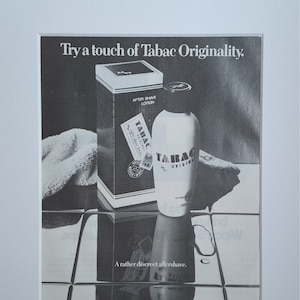 May include: Black and white photograph advertising Tabac Original aftershave. The ad shows a bottle of aftershave and a box of aftershave lotion. The text on the ad reads "Try a touch of Tabac Originality." and "A rather discreet aftershave."