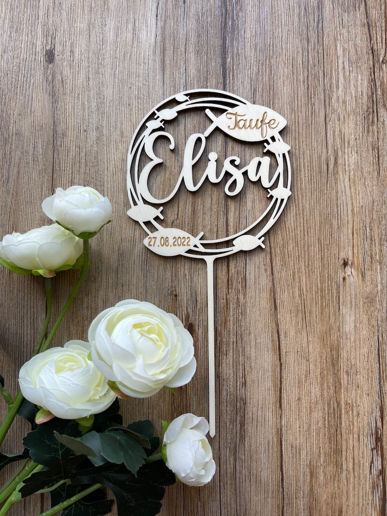 Może przedstawiać: Drewniany znak z okrągłym wzorem przedstawiającym symbol ryby i słowo "Taufe" oraz imię "Elisa" z datą "27.08.2022".