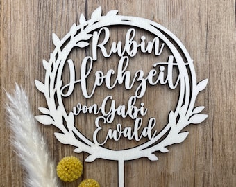 May include: A white wooden cake topper with a wreath design and the text "Rubin Hochzeit von Gabi Ewald".