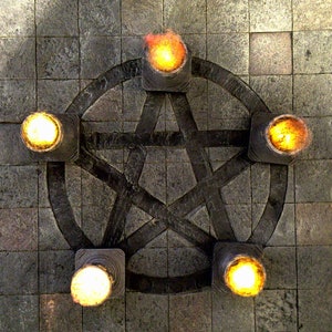 May include: A dark gray pentagram design with five illuminated torches. The torches have a square base and emit a bright yellow-orange light. The background is a textured, gray stone surface.