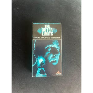 May include: A VHS tape for "The Outer Limits" featuring Ed Asner in "It Crawled Out of the Woodwork." The cover has a blue and black design with a man's face and a figure in a doorway. The MGM/UA logo is at the bottom.