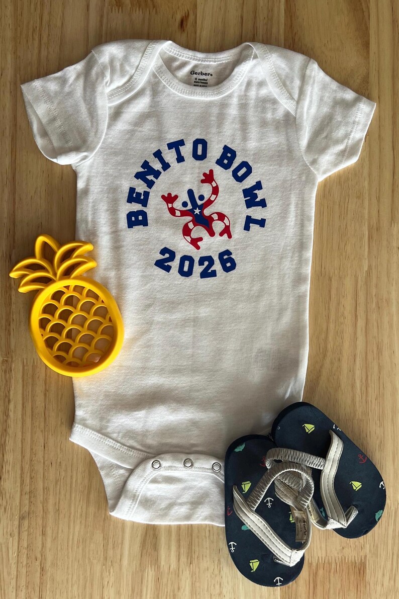 Op de afbeelding: Witte babybody met de tekst "BENITO BOWL 2026" in blauw, met een rood-blauwe afbeelding. Een geel ananasvormig speelgoed en marineblauwe teenslippers met anker- en zeilbootontwerpen zijn ook in de afbeelding.